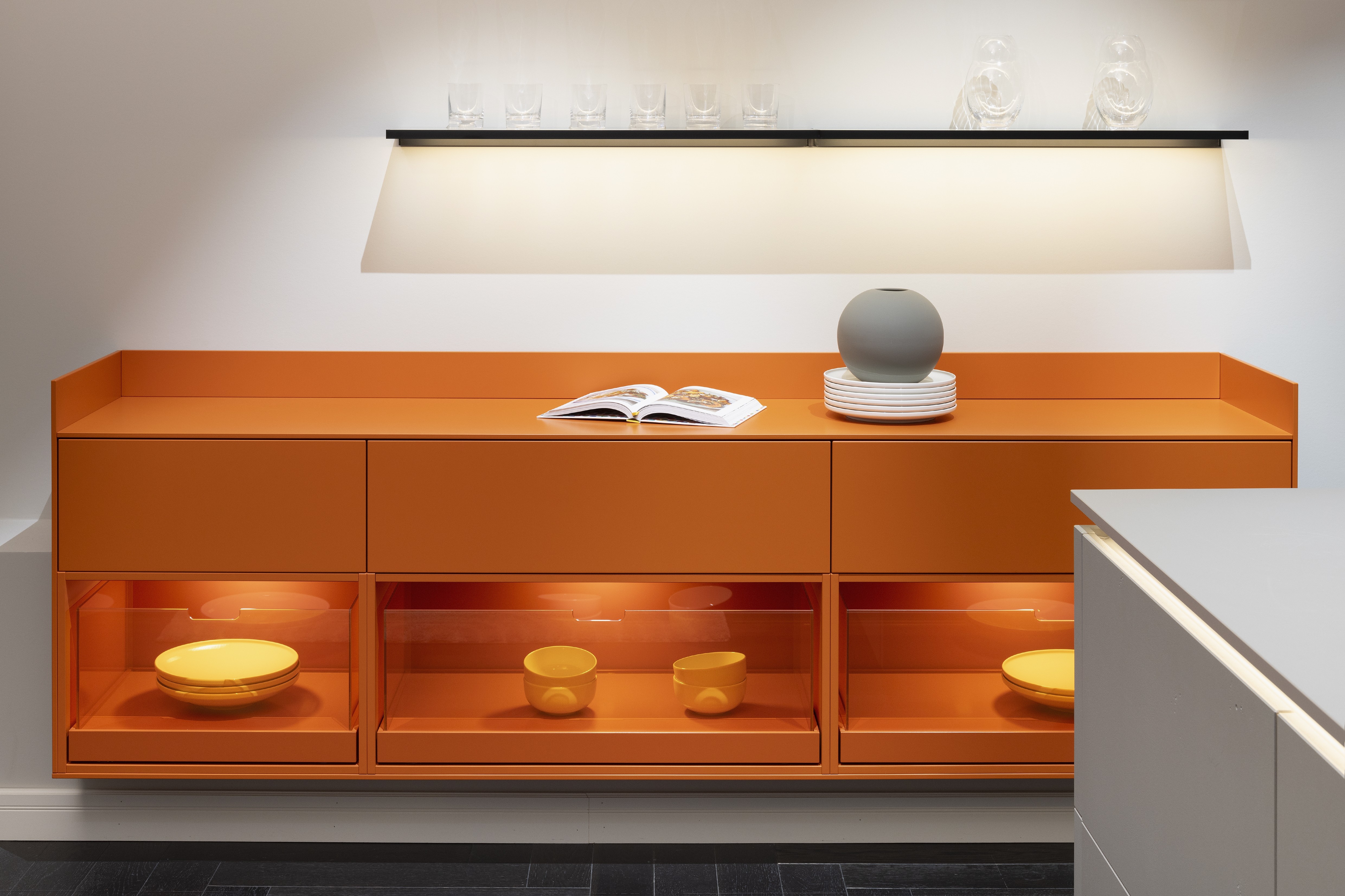 APL: 171 Greige 16 mm Front: AV 7010-GL Beton-grau, mineralischer Spachtelbeton (PUResist, PURemmision) Front Lack Orange Korpus: 2059 Designkorpus Titan Griff: Metall Black Chrome und Kehlleiste 359 Greige matt Kehlleiste Graphit gebürstet Geräte: Gaggenau Armatur: Franke Spüle: Franke  Features: Betonoberfläche individuell nachbearbeitet, Nischenrückwand Regal Betonoberfläche, Sideboard Orange mit offenen Schubkästen in Plexiglas Orange exklusives Auszugssystem im Schrank für mehr Stauraum, Sideboard 